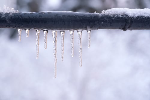 Frozen icicles on a gray pipe